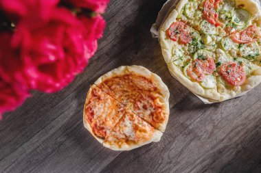 Tahta bir masada, tepside, bir buket gülle iştah açıcı pizza. Yemek ve eğlence kavramı.