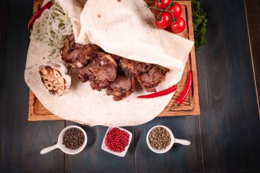 İştah açıcı kızarmış et, ahşap bir tepside, baharatların arasında yatıyor. Yemek endüstrisindeki yemek fotoğrafçılığı, karanlık arka plan.