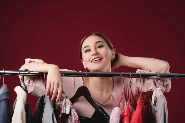 Menina bonita escolhe e experimenta roupas em um fundo vermelho. O conceito de escolher e comprar roupas, shopaholism e consumismo — Fotografia de Stock