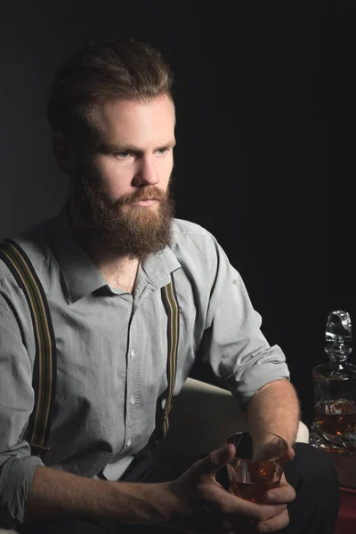 Портрет задумчивого красивого молодого человека со стаканом алкоголя в руках, на изолированном черном фоне. Концепция времяпрепровождения, отдыха и отдыха — стоковое фото