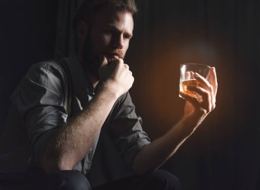 Sakallı yakışıklı bir genç adam elinde bir bardak alkolle karanlık bir odada oturuyor. Dinlenme, rahatlama, içki ve yalnızlık kavramı.