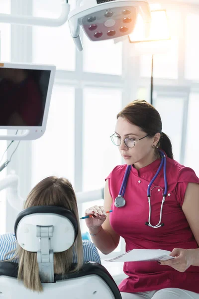 The dentist consults a patient sitting in a chair in the dental office. The concept of health, dental services and healthcare