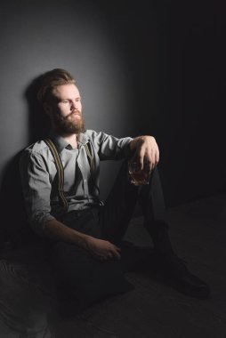 Sakallı yakışıklı bir genç adam elinde bir bardak alkolle karanlık bir odada oturuyor. Dinlenme, rahatlama, içki ve yalnızlık kavramı.