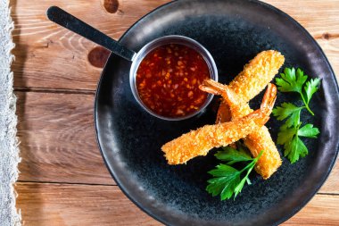 Sos ve otlarla dolu ahşap bir masada, karanlık bir tabakta iştah açıcı kızarmış karides. Yemek, servis, bar ve restoran kavramı