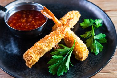 Sos ve otlarla dolu ahşap bir masada, karanlık bir tabakta iştah açıcı kızarmış karides. Yemek, servis, bar ve restoran kavramı