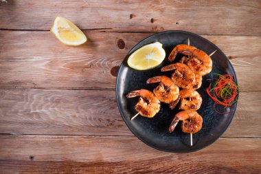 Tahta bir yüzey üzerinde, limon ve baharatların arasında siyah bir tabakta iştah açıcı kızarmış karides. Hızlı ve sağlıklı yemek kavramı.