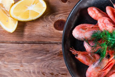 İştah açıcı haşlanmış karides siyah bir tabakta, ahşap bir yüzey üzerinde limonun arasında. Hızlı ve sağlıklı yemek kavramı.