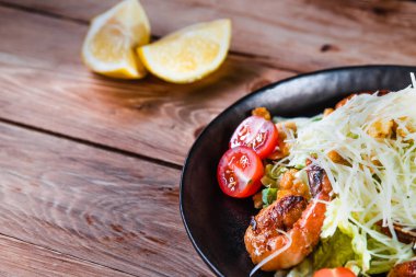 İştah açıcı Sezar salatası, siyah bir tabakta karides, ahşap bir masada, limonun yanında. Sağlıklı yemek ve hizmet kavramı