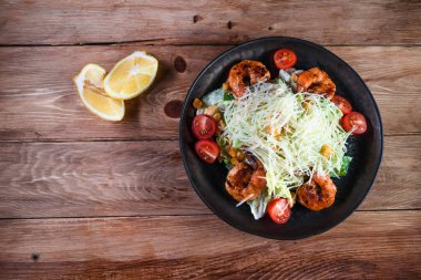 İştah açıcı Sezar salatası, siyah bir tabakta karides, ahşap bir masada, limonun yanında. Sağlıklı yemek ve hizmet kavramı
