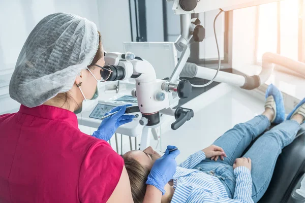 El médico dentista mira con un microscopio los dientes del paciente. El concepto de atención y tratamiento de la salud en las instalaciones médicas — Foto de Stock
