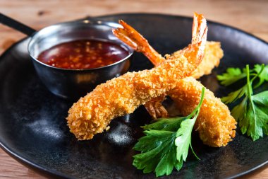 Sos ve otlarla dolu ahşap bir masada, karanlık bir tabakta iştah açıcı kızarmış karides. Yemek, servis, bar ve restoran kavramı