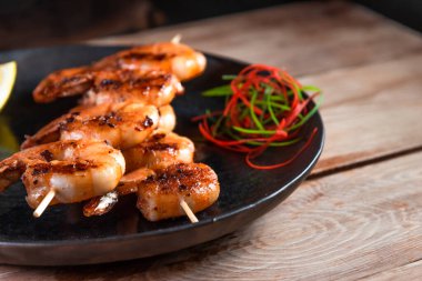 Tahta bir yüzey üzerinde, limon ve baharatların arasında siyah bir tabakta iştah açıcı kızarmış karides. Hızlı ve sağlıklı yemek kavramı.