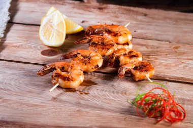 Tahta bir yüzeyde, limon ve baharatların arasında şişte iştah açıcı kızarmış karides. Hızlı ve sağlıklı yemek kavramı.