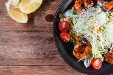 İştah açıcı Sezar salatası, siyah bir tabakta karides, ahşap bir masada, limonun yanında. Sağlıklı yemek ve hizmet kavramı
