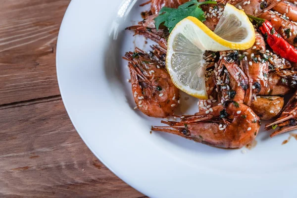 Camarão frito apetitoso com especialidades, sementes de sésamo e limão, em uma chapa branca em um fundo de madeira. Conceito de comida em restaurantes e bares — Fotografia de Stock