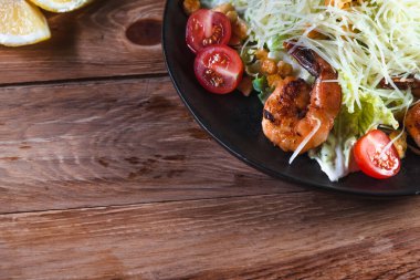 İştah açıcı Sezar salatası, siyah bir tabakta karides, ahşap bir masada, limonun yanında. Sağlıklı yemek ve hizmet kavramı
