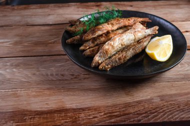 Siyah bir tabakta iştah açıcı kızarmış kapelinler ahşap bir yüzey üzerinde duruyor. Basit kırsal gıda konsepti.