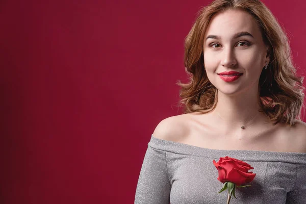 Menina bonita com maquiagem brilhante, segurando uma rosa em suas mãos em um fundo vermelho no estúdio. O conceito de juventude, beleza e um corpo saudável — Fotografia de Stock