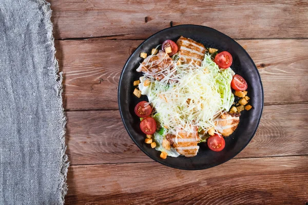 把凯撒沙拉和鸡肉放在木桌上的黑色盘子里吃.健康食品和服务的概念 — 图库照片