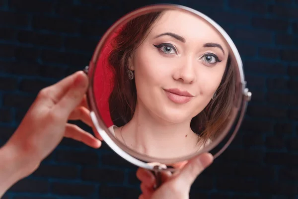 Uma jovem atraente olha-se ao espelho. O conceito de juventude, beleza e cuidado pessoal — Fotografia de Stock