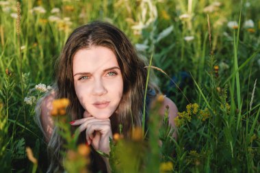 Mavi uzun elbiseli güzel sarışın bir kadın çiçeklerle dolu bir tarlada yatıyor. Güzellik, özgür yaşam ve doğallık kavramı.