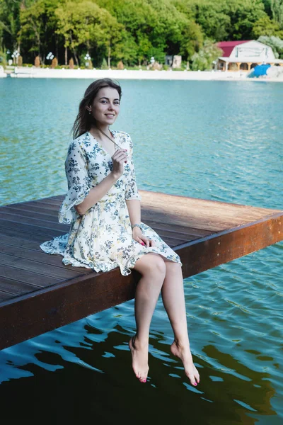 Una mujer hermosa y sexy, con el pelo largo en un vestido de verano, pasa tiempo en la orilla del lago, rodeado de bosques y montañas. Concepto de descanso y relajación — Foto de Stock