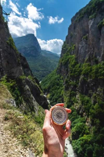 First-person view of a female hand with a compass on a background of a beautiful mountain landscape. The concept of navigating the search for your own path and orientation to the cardinal points