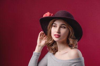 Kırmızı arka planda şapkasını düzelten güzel bir kadının portresi. Güzellik ve gençlik kavramı