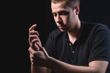 Siyah gömlekli genç yakışıklı bir adam oturur ve siyah bir arka planda elini ovuşturur. Sağlık ve kişisel bakım kavramı