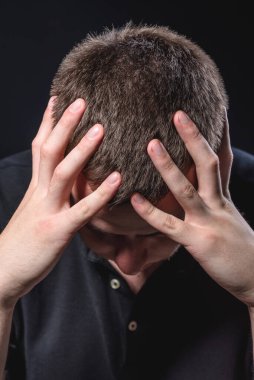 Siyah gömlekli genç yakışıklı adam oturur ve başını siyah bir arka planda tutar. Stres ve acı hissediyorum.