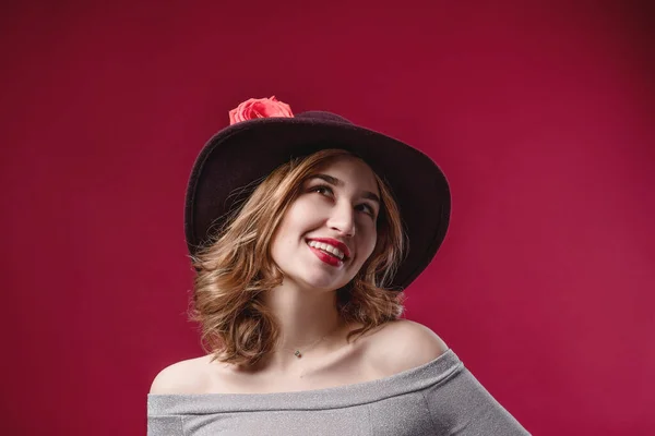 Retrato de uma bela mulher que endireita um chapéu sobre um fundo vermelho. O conceito de beleza e juventude — Fotografia de Stock