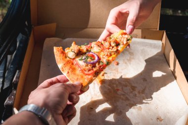 Güzel, genç bir kadın sokakta pizza ve patates kızartması yiyor. Fast food, yemek teslimatı ve doğada öğle yemeği kavramı.