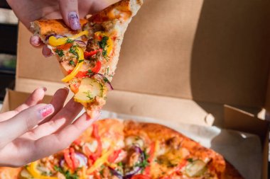 El ele tutuşup kutudan bir dilim pizza alıyoruz. Fast food, yemek teslimatı ve doğada öğle yemeği kavramı.