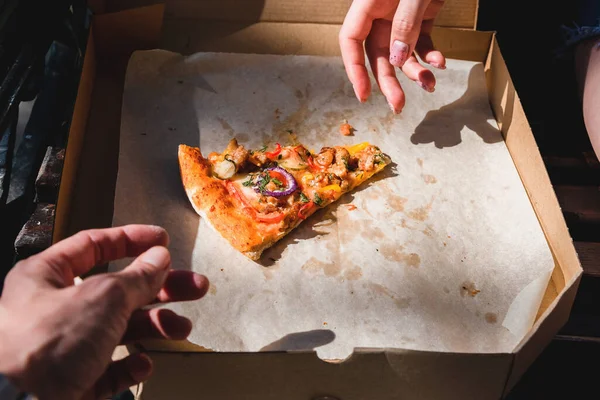 El ele tutuşup kutudan bir dilim pizza alıyoruz. Fast food, yemek teslimatı ve doğada öğle yemeği kavramı.