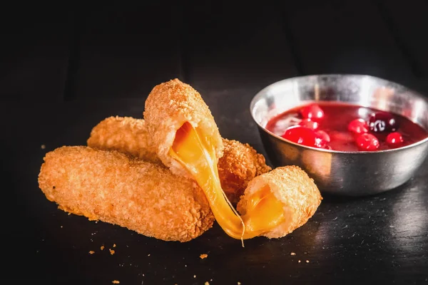 Fried cheese sticks in breading with berry sauce on a black background. Ready food and fast food concept