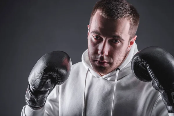 Jeune homme en gants de boxe et un sweat-shirt blanc sur fond sombre dans le studio. Le concept de victoires et de batailles — Photo