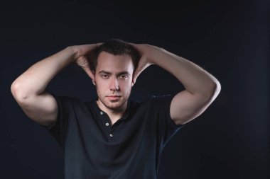 Siyah polo tişörtlü yakışıklı bir genç stüdyonun arka planında başını tutuyor.