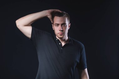 Siyah polo tişörtlü yakışıklı bir genç stüdyonun arka planında başını tutuyor.