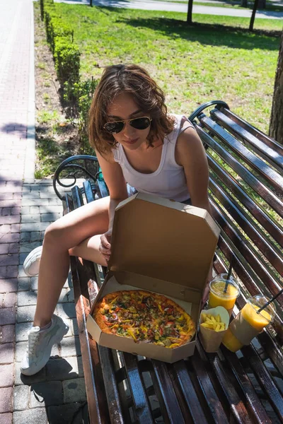 Sokakta pizza yiyen güzel, genç bir kadın. Fast food, yemek teslimatı ve doğada öğle yemeği kavramı.