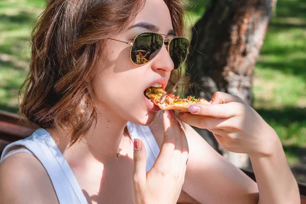 Uma jovem linda a comer pizza na rua. O conceito de fast food, entrega de alimentos e almoço na natureza — Fotografia de Stock