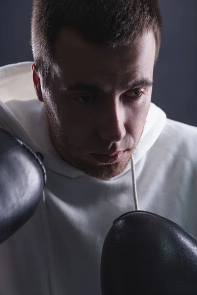 Νεαρός με γάντια μποξ και λευκό φούτερ σε σκούρο φόντο στο στούντιο. Η έννοια των νικών και των μαχών — Φωτογραφία Αρχείου