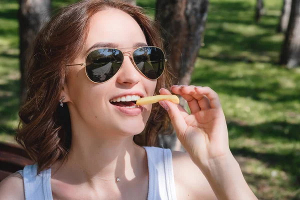Uma jovem linda a comer batatas fritas na rua. O conceito de fast food, entrega de alimentos e almoço na natureza — Fotografia de Stock