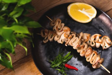 Limonlu şiş üzerinde kızarmış kalamar bbq siyah bir tabakta yatıyor. Restoran yemeği ve servis konsepti