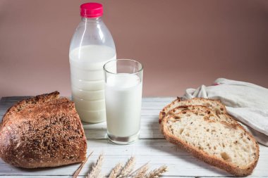 Beyaz bir tahta üzerinde bir bardak süt, dilimlenmiş köy ekmeği ve reçel. Sağlıklı gıda ve tarım kavramı