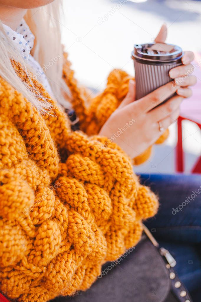 Woman in orange knitted bubbles cardigan holding cup of coffee