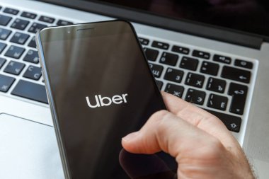 Moskova / Rusya Federasyonu - 13 Mart 2019: erkek elinde siyah bir iphone, Uber logonun ekranıdır. Macbook arka plan üzerinde