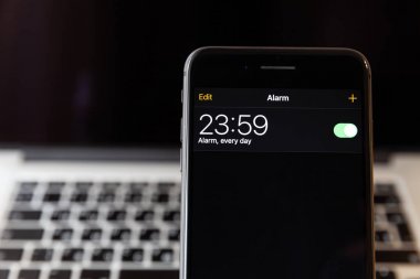 Moskova/Rusya-13 Nisan 2019: siyah iPhone 8 Plus MacBook arka planda. Çalar saat 23:59 için ayarlanır