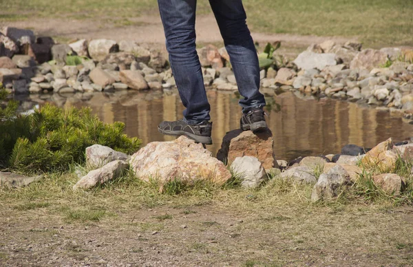 man\'s feet standing on the rocks near the pond