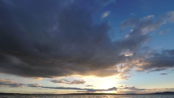 De zon gaat over de horizon, de wolken zijn snel in de lucht. Zonsondergang in timelapse bij het meer. — Stockvideo