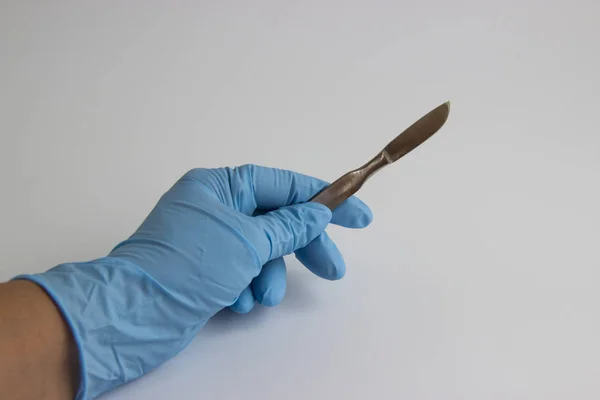Рука хірурга в синій медичній рукавичці, що тримає скальпель ізольовано на білому тлі — стокове фото